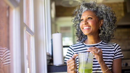 Woman next to window, looking out, drinking green smoothy