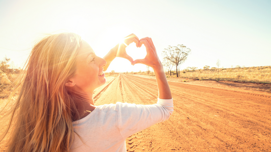 Woman on a sunny desert road, hands making a heart shape