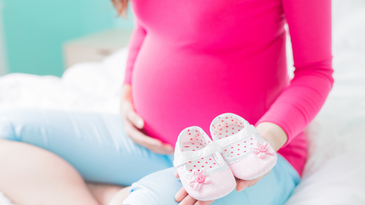 Pregnant woman sitting on bed and holding baby shoes